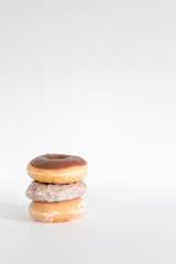 Three donuts stacked on one another, chocolate iced, blueberry cake, and plain glaze, white background, copy space