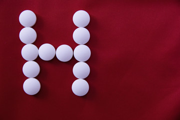 White round medical pills lie on a red background in the form of a letter H