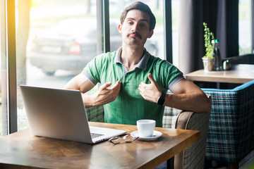 This is me! Young proud haughty businessman in green t-shirt sitting with laptop and looking at...