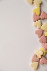 pink and yellow Vitamins in the shape of a heart lie on a white background in equal order on one side of the sheet leaving an empty spot