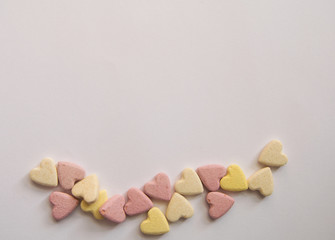 pink and yellow Vitamins in the shape of a heart lie on a white background in equal order on one side of the sheet leaving an empty spot