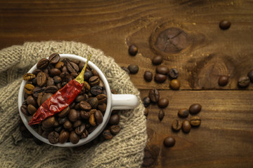 Cup with chili pepper and coffee grains on wooden table