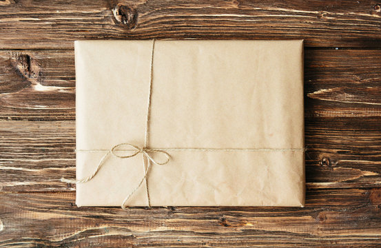 Overhead view of a single holiday package wrapped with eco friendly craft paper and tied with twine. Square format on a rustic wooden table.