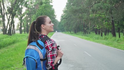 Happy female backpacker admiring nature, walking on countryside road. Rear view shot of a cheerful woman enjoying backpacking, looking around. Tourism, vacation concept