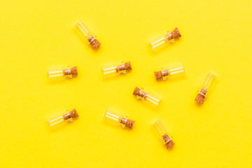 Small empty transparent bottles with corks are laid out randomly on a yellow background. Top view
