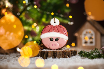Fototapeta na wymiar Holiday traditional food bakery. Gingerbread pink pig head in hat in cozy warm decoration with garland lights