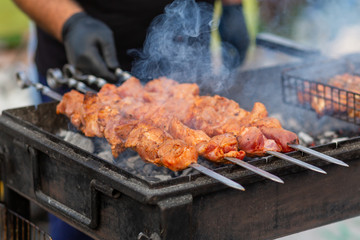 The cook fries juicy steaming meat on a charcoal grill. Food and cooking equipment at a street food festival