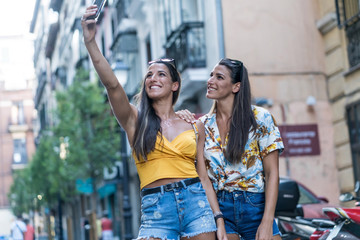 Pretty twin sisters taking a selfie in the street on a sunny day.