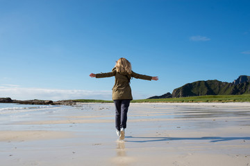 Blond hair girl running along the empty sandy ocean beach. Summer in North. Happy women. Beautiful nature landscape. Scenic outdoor view. Enjoy the moment, relaxation. Wanderlust. Travel, adventure