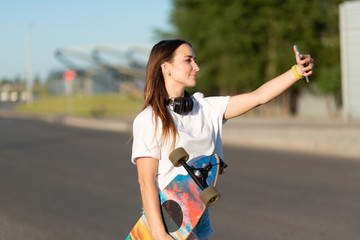 Girl walking with longboard and make selfie on mobile phone