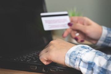 A woman buys goods in an online store. Female hands is holding a credit card on a laptop background.