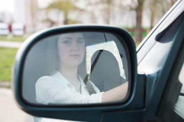 The girl goes behind the wheel of a car and looks in the side mirror. Woman driving.