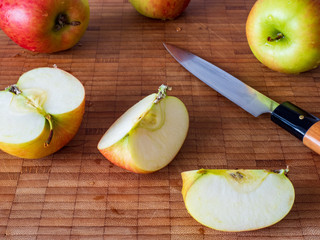 Mehrere Äpfel mit geschnittenen Apfelstücken mit Messer auf Holzbrett