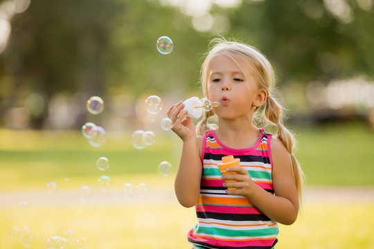 little blonde girl inflates soap bubbles in summer on a walk,  International children's day