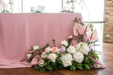 The wedding table setting for the newlyweds is decorated with fresh flowers of carnation, rose, anthurium and eucalyptus leaves. Silver candlesticks, white candles. Wedding floristry. Closeup details