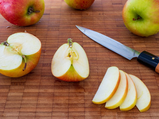 Mehrere &Auml;pfel mit geschnittenen Apfelst&uuml;cken und Apfelscheiben mit Messer auf Holzbrett