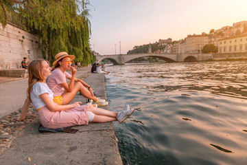 Two happy caucasian and asian girls friends meeting great sunset on a river Saone in Lyon city....
