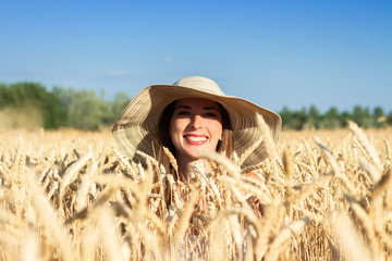 Young woman in a wide-brimmed hat peeks out of wheat, a field of wheat