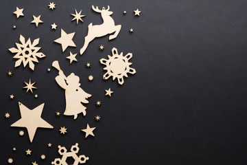 Wooden handmade Christmas decorations on dark black background. Christmas snowflakes, deer, angel, stars with copy space. Flat lay, top view. Winter holidays, Christmas, New Year banner mockup