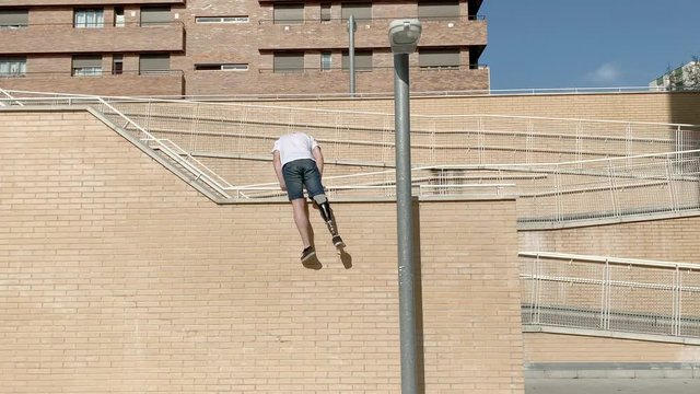 Young man with orthopedic leg prosthesis jumping between buildings practicing parkour