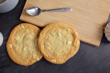 Top view of white chocolate chips cookies on black marble background with cutting board and spoon