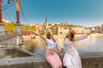 Two happy girls friends walking on Saint Georges pedestrian bridge while traveling in Lyon old town...