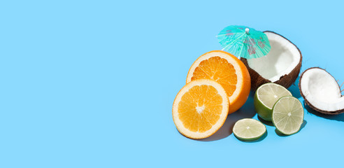 Fresh juicy orange, coconut and green lime with a cocktail umbrella isolated on blue background. Concept of Healthy eating and dieting. Travel and holiday concept