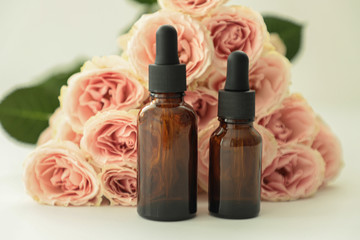 Dark cosmetic bottles, with pink roses on a whait background. Copy space. Friendly natural cosmetics concept. Minimalism. Beauty blogger, spa salon, terapy salon.
