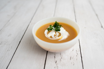 Pumpkin soup with sour cream in white small bowl 
