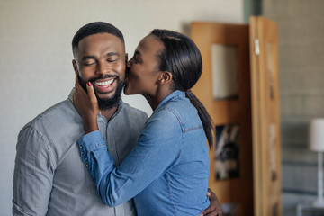 Loving African American wife kissing her husband on the cheek - obrazy, fototapety, plakaty