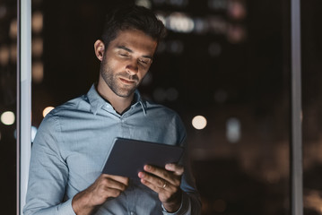 Handsome businessman using a tablet in his office at night - Powered by Adobe