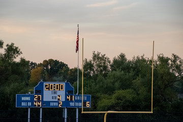 Football end zone with goal posts, Amercian flag and score board during evening sunset at local high school