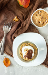 Carrot op pumpkin mug cupcake with whipped cream, caramel sauce and walnuts in a white ceramic mug. Cozy autumn or winter breakfast. Healthy dessert. 