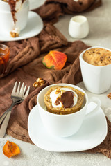 Carrot op pumpkin mug cupcake with whipped cream, caramel sauce and walnuts in a white ceramic mug. Cozy autumn or winter breakfast. Healthy dessert. 