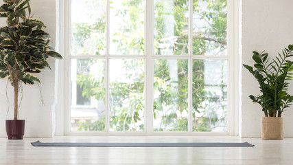 Empty yoga studio interior with windows and unrolled mat