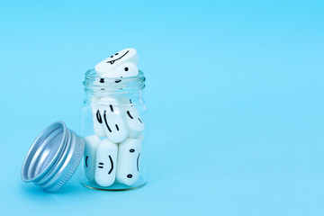  Pills with funny faces and a glass bottle on a blue background. Pharmacy antibiotic. Treating with antidepressant. Mental disorder. The concept of antidepressants and healing. Copy space.