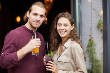 Waist up portrait of beautiful young couple drinking cocktails while posing outdoors standing by cafe, copy space