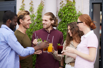 Multi-ethnic group of people enjoying cold drinks and chatting cheerfully during outdoor Summer party, copy space