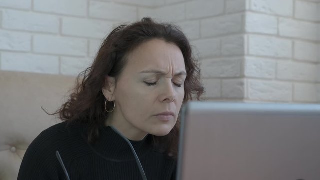 Woman have problem with eyes. A woman with poor eyesight puts on glasses and works on a laptop.