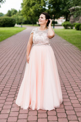 Brunette caucasian model in elegant floor-length pink dress dreamy looking away in park.