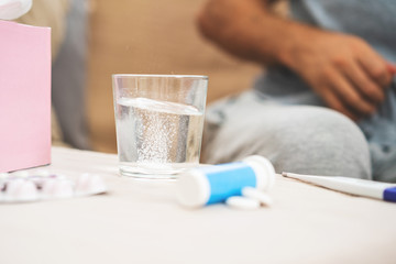 Water With Soluble Tablet For An Ill Patient. Healthcare, Traditional Medicine And Flu Concept - Man Takes Pill from Headache Sitting On Sofa. Sick man treating symptoms caused by cold or flu.