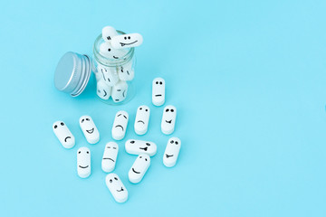  Pills with funny faces and a glass bottle on a blue background. Pharmacy antibiotic. Treating with antidepressant. Mental disorder. The concept of antidepressants and healing. Copy space.