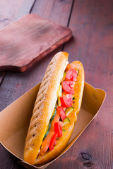 Grilled sandwich with vegetables in paper box. Sandwich with tomatoes and cucumbers on wooden boards. Copy space
