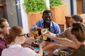 Multi-ethnic group of friends toasting while enjoying dinner together during party in cafe, focus on smiling African-American man, copy space