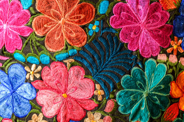 Background of hand-embroidered flowers on a fabric with colored threads.