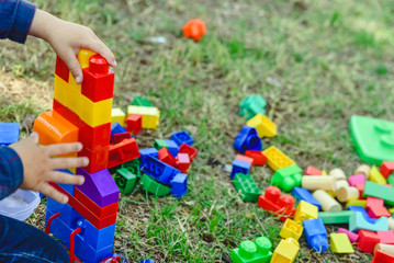 Child playing with colorful blocks sitting on the ground of a garden in spring, negative space.