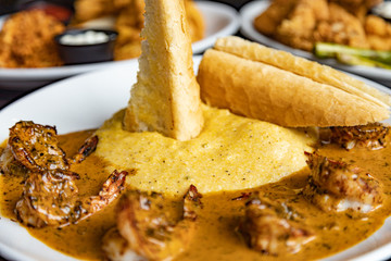 Crispy bread stuck in the grits and shrimp creole cuisine on a white plate. Close up with other platters blurred in the background