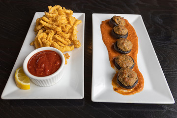 Two long white platters of appetizers on a black tabletop. Calamari with a red dipping sauce and alligator stuffed mushrooms in alligator piquant sauce.