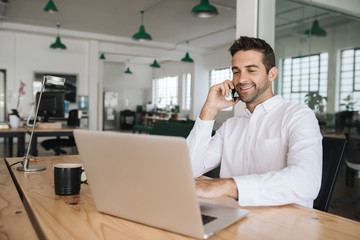 Smiling businessman sitting at his desk talking on a cellphone