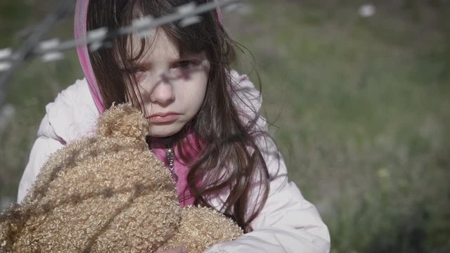 Child miss parents. Orphan child with a teddy bear. Sad homeless little girl with a teddy bear behind a barbed wire.